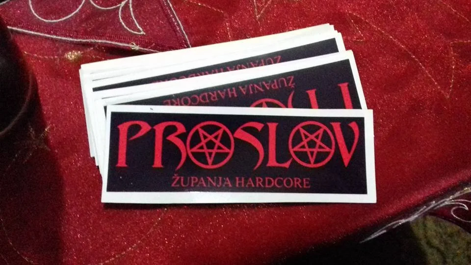 A stack of black stickers with red text reading "PROSLOV" and featuring a pentagram in the second 'O', placed on a red, glittery tablecloth.