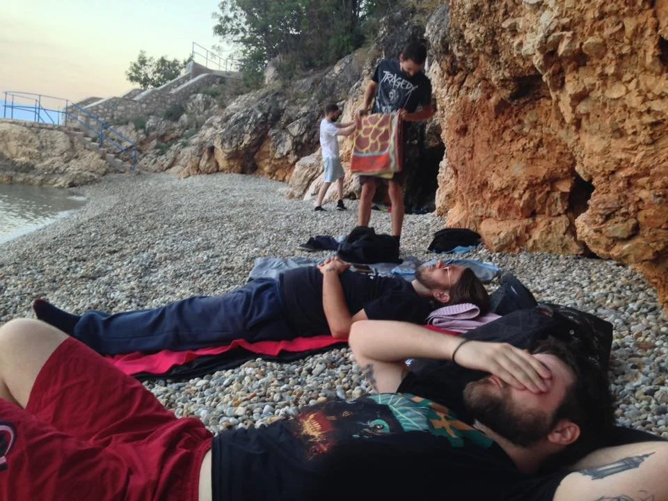 People relaxing on a pebbled beach near rocky cliffs.