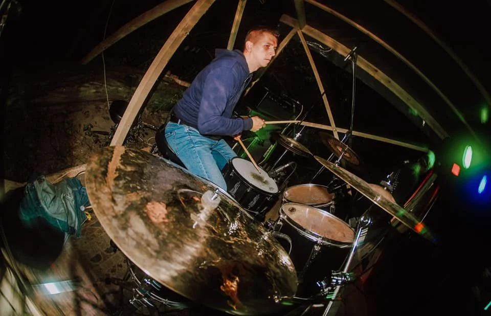 A person playing drums in a dimly lit environment with colorful lights.