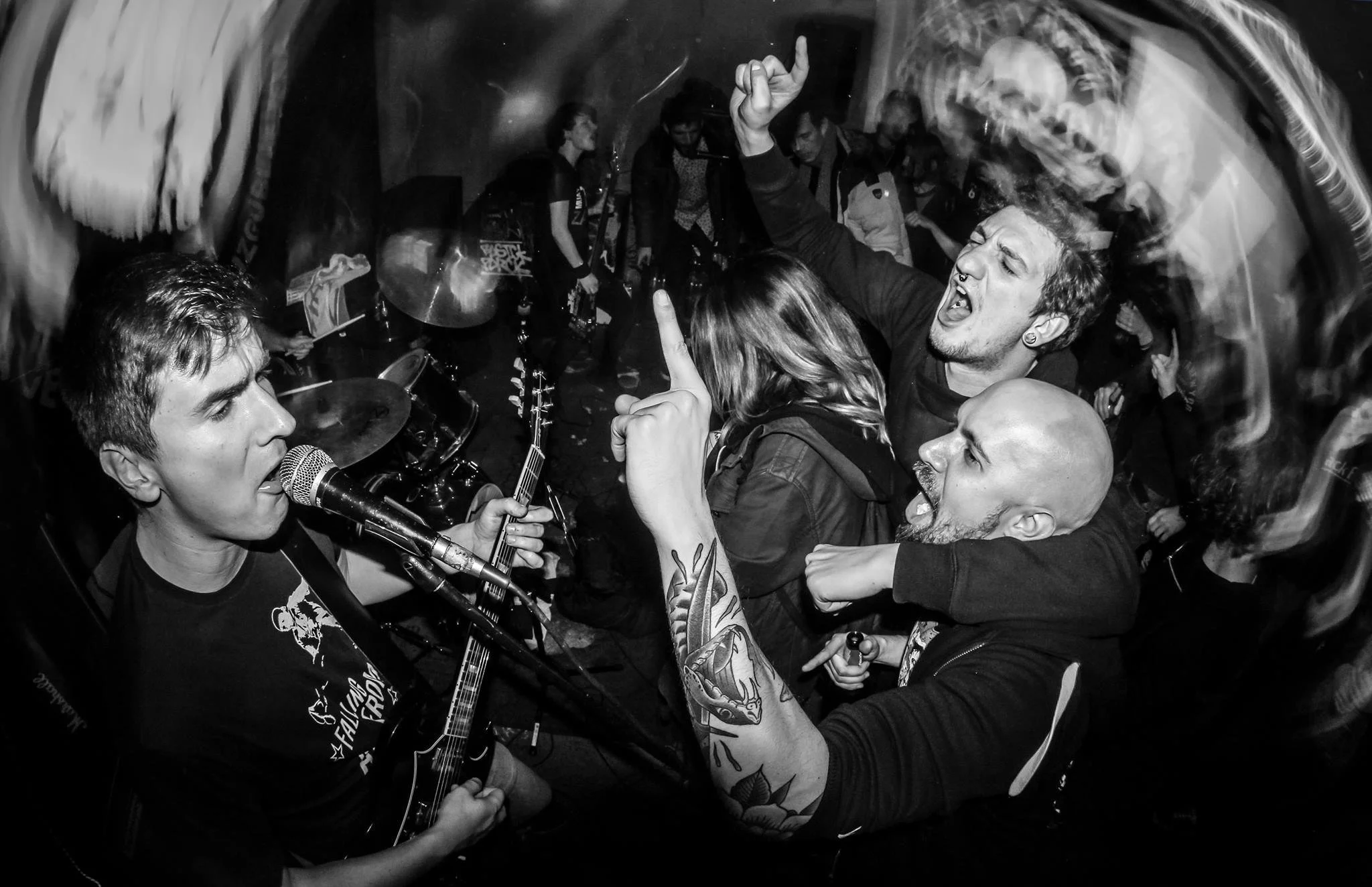 Black and white photo of a lively crowd at a music concert, with a singer playing guitar and singing into a microphone, surrounded by fans dancing and enjoying the performance.