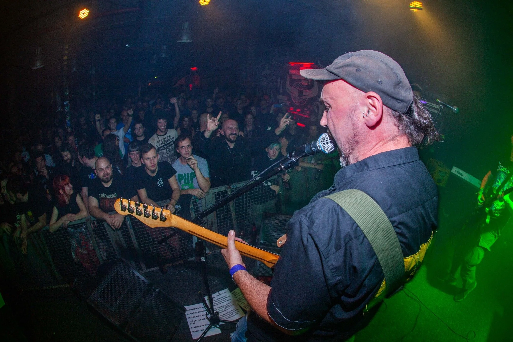 A musician playing an electric guitar on stage at a concert, with a crowd of people watching and cheering in the background.