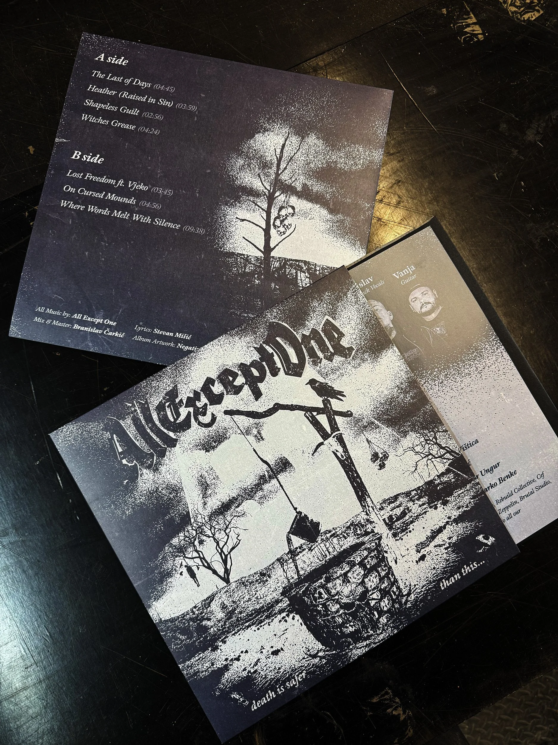 A black and white concert setlist with song titles, durations, and credits, placed on a dark surface, alongside a partially visible flyer with artwork and band members' photos.