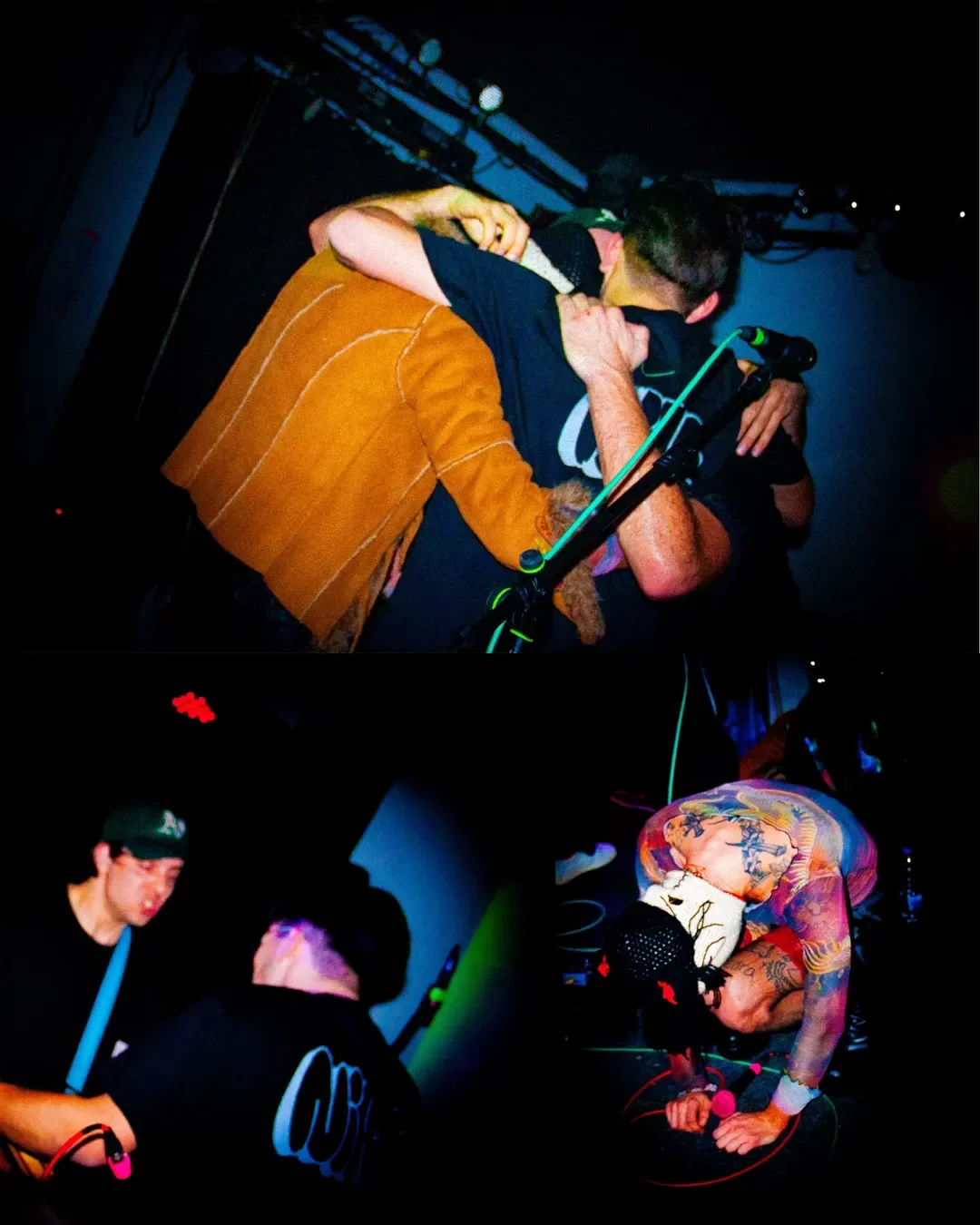 Two men hugging on stage with a microphone, one wearing a brown suede jacket and the other a black T-shirt, in a dark setting with stage equipment visible.