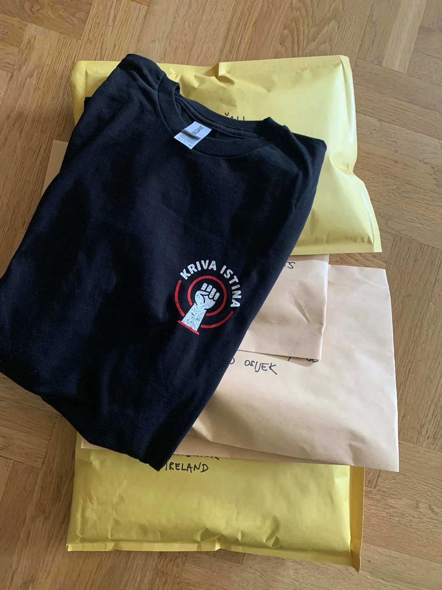 A black t-shirt with a circular logo and text is placed on top of yellow and white papers on a wooden surface.
