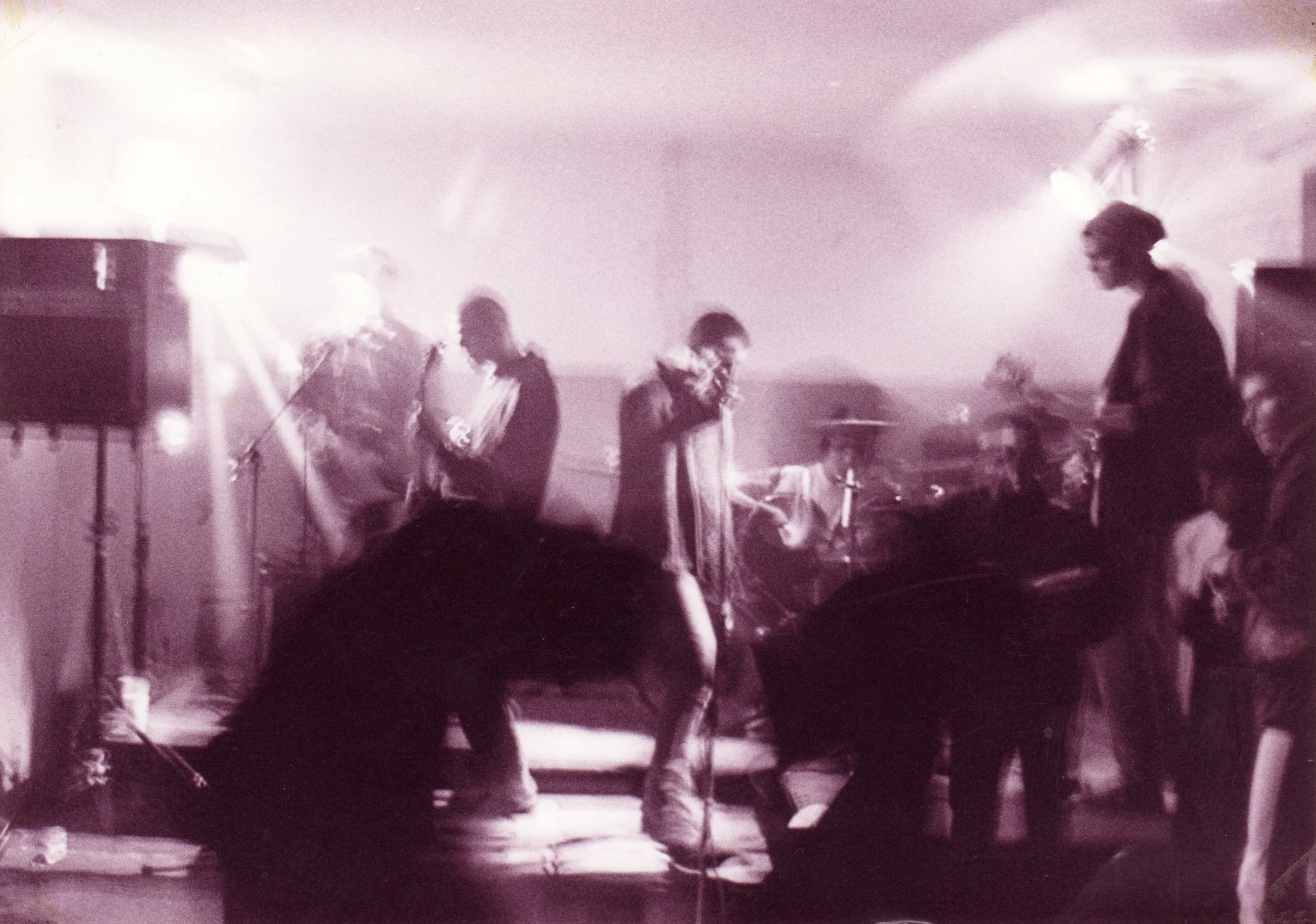 A band performing live on stage with four musicians, playing instruments and singing into microphones, under stage lighting.