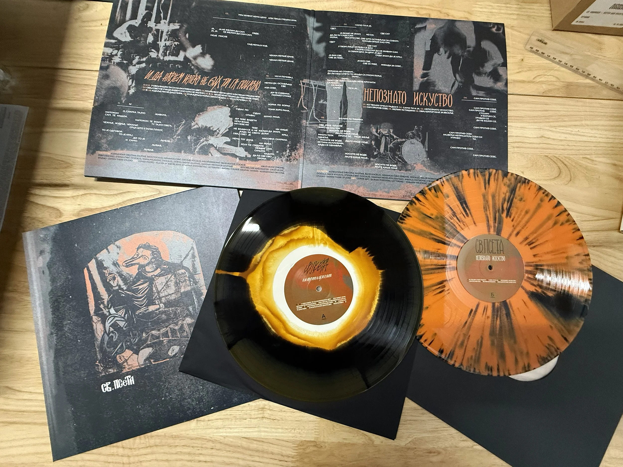 Colored vinyl records with black booklets and a black-and-white poster on a wooden surface.
