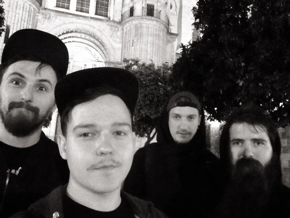 Four young men taking a selfie outdoors at night in front of a historic building with ornate architecture and a large tree.