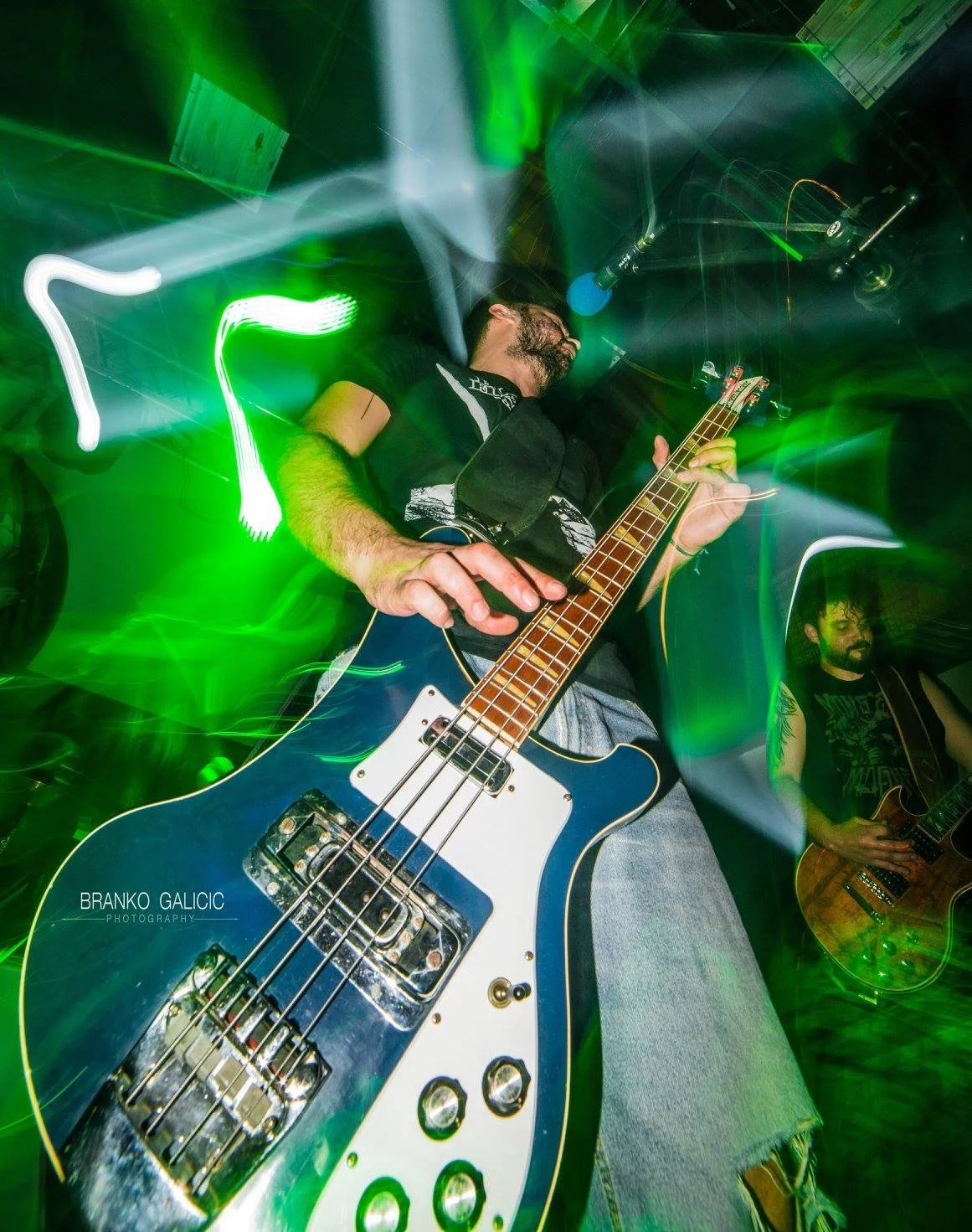 Musician playing a bass guitar on stage with green and white lights creating a dynamic background