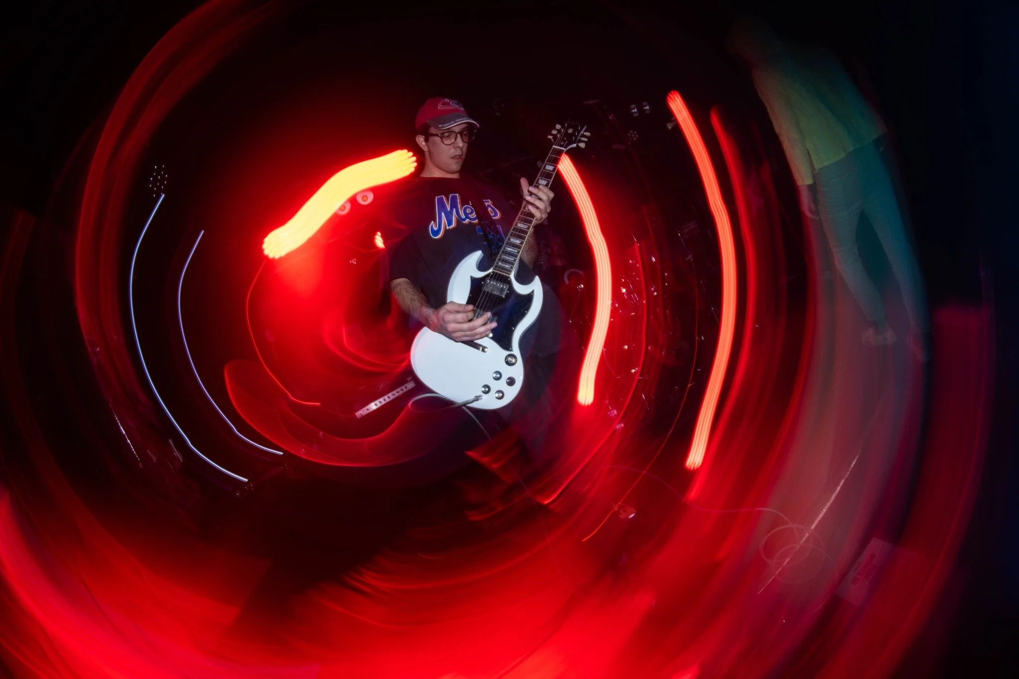 Person playing an electric guitar on stage with colorful light trails surrounding them.