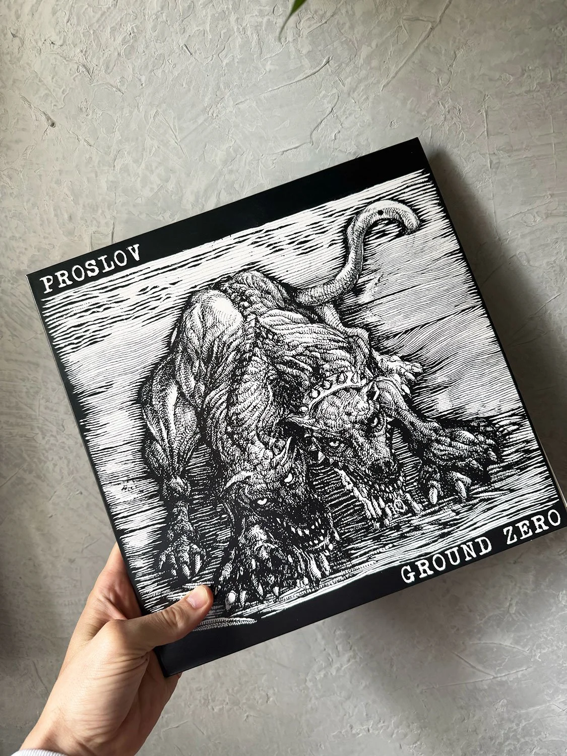 Black and white illustration of a fierce, monstrous dog with a spiked collar, crouching in water, with the words 'Proslov' and 'Ground Zero' on the edges.