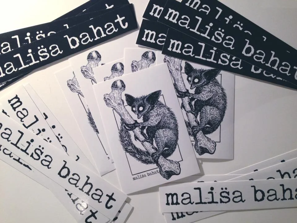 Printed stickers with the name "Mališa Bahat" in white text on black background and black text on white background, as well as illustrated black and white drawings of a fox sitting on a tree branch, labeled with the name "Mališa Bahat."