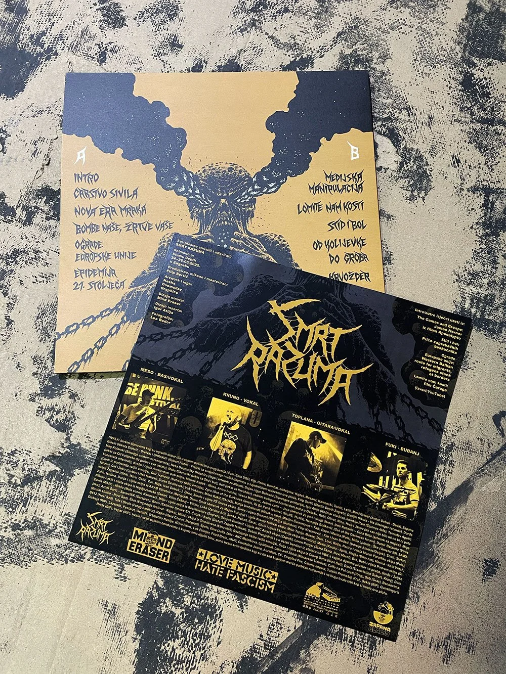 Two black posters with yellow and white text and images, featuring a graphic of a muscular man with a yellow background and a dark-themed, heavy-metal style font. The posters are placed on a textured surface with black and white splatters.
