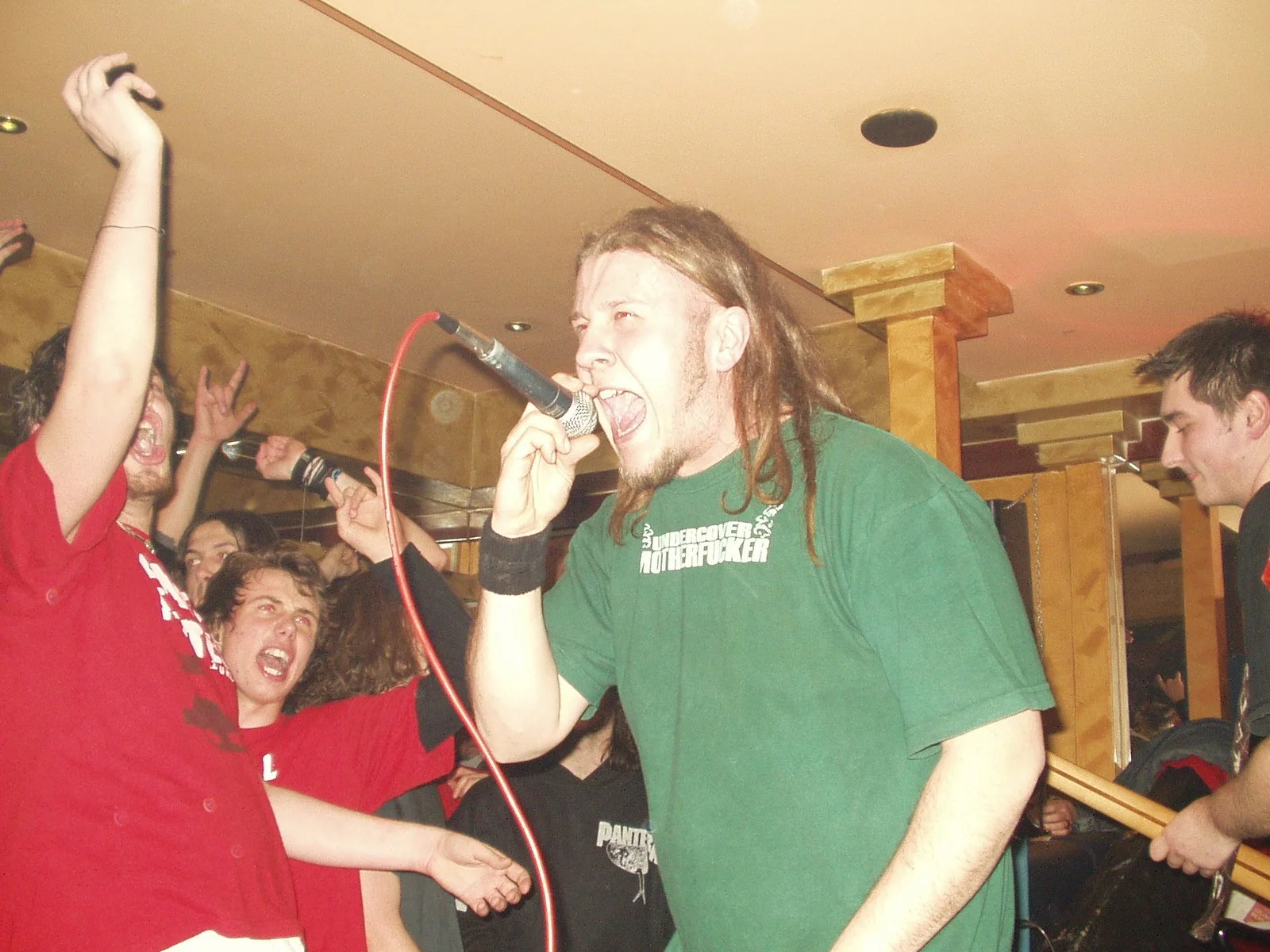 A man with long dreadlocks singing into a microphone at a lively concert or party with people around him cheering.