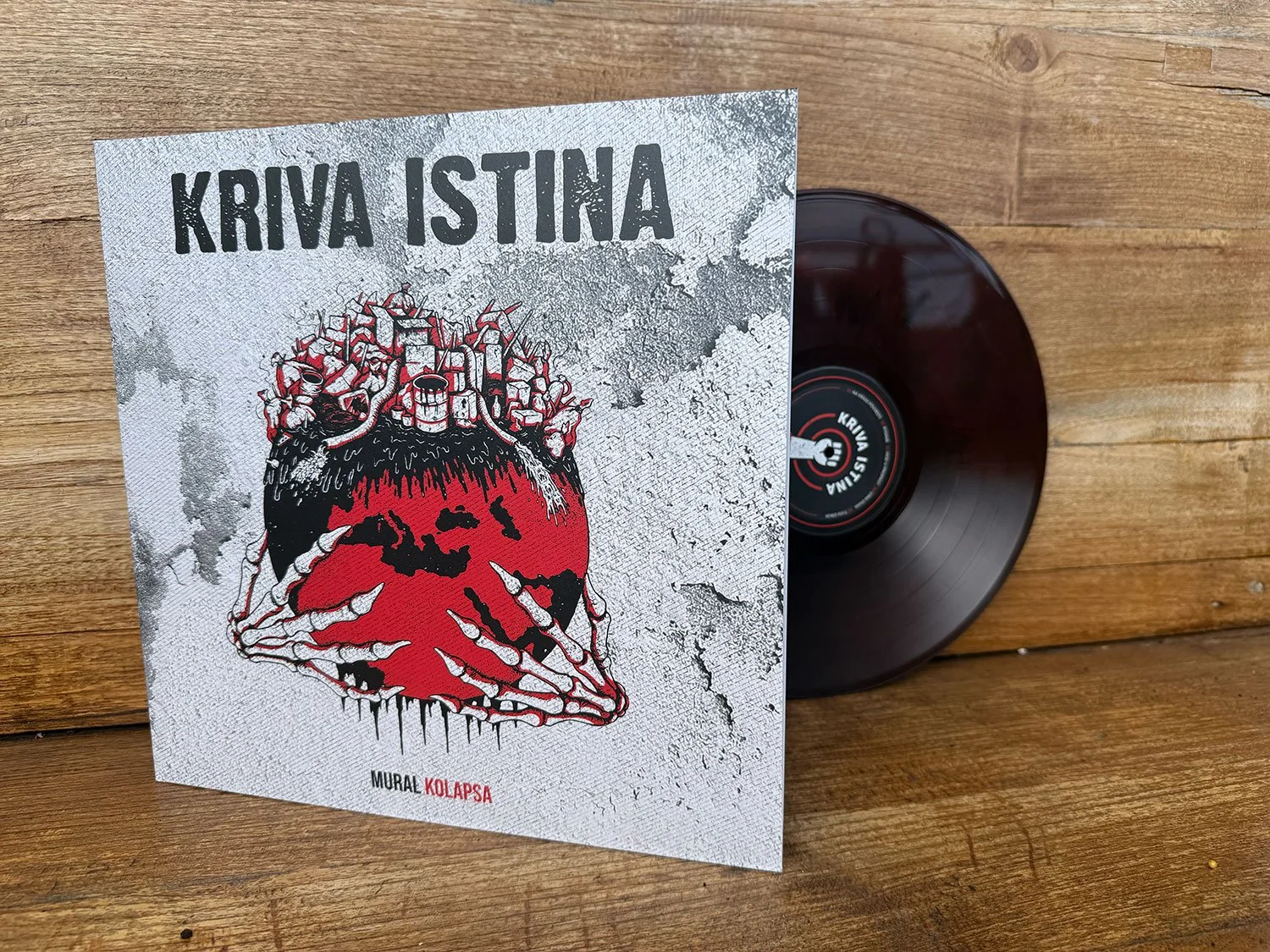 Vinyl record and album cover titled 'KRIVA ISTINA.' The album cover features an illustration of a red human heart with skeleton hands holding it, surrounded by a cracked, textured background. The text on the cover includes 'MURAL KOLAPSA.'