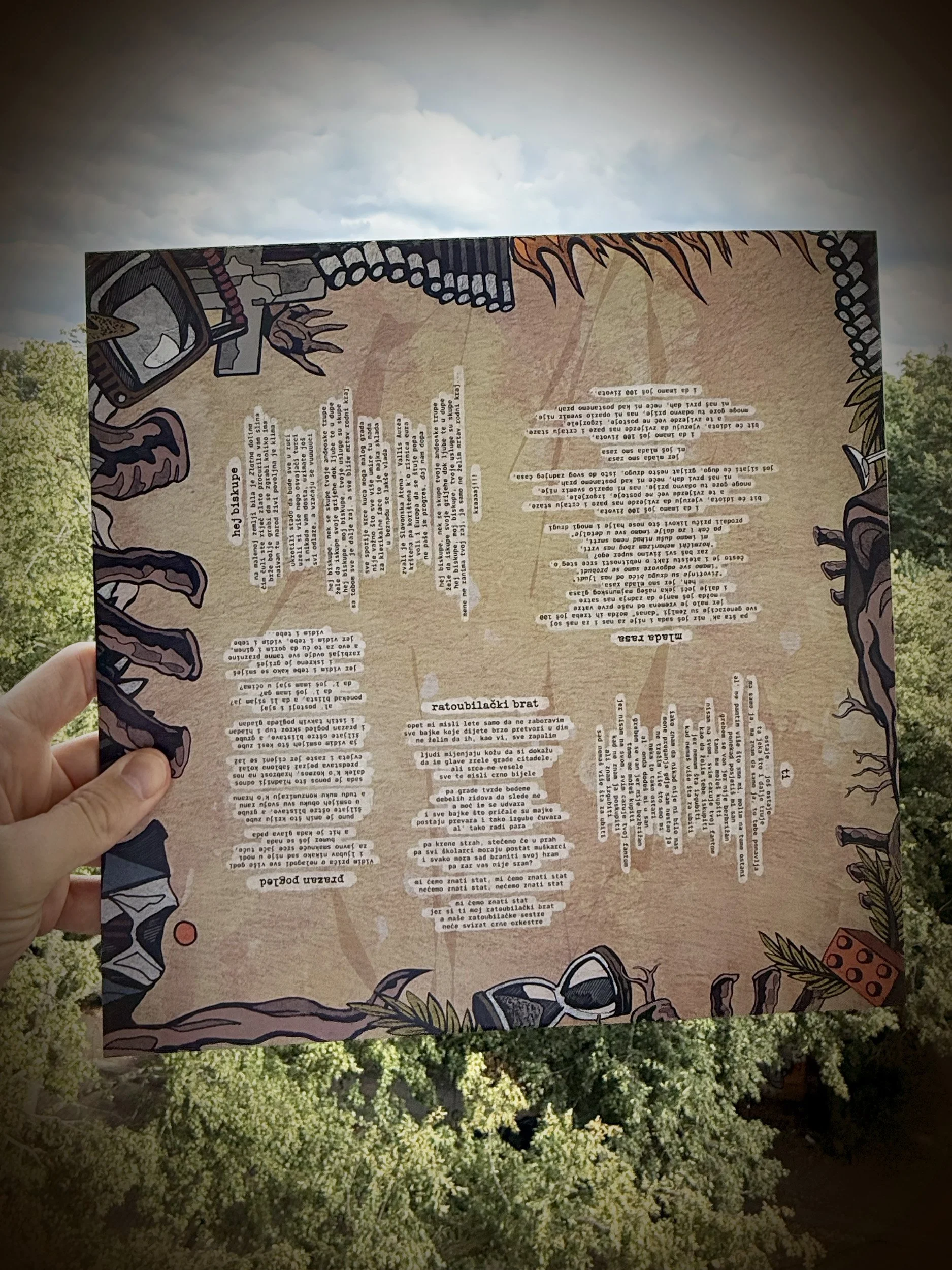 A person holding a piece of paper with text, outdoors with trees and a cloudy sky in the background.