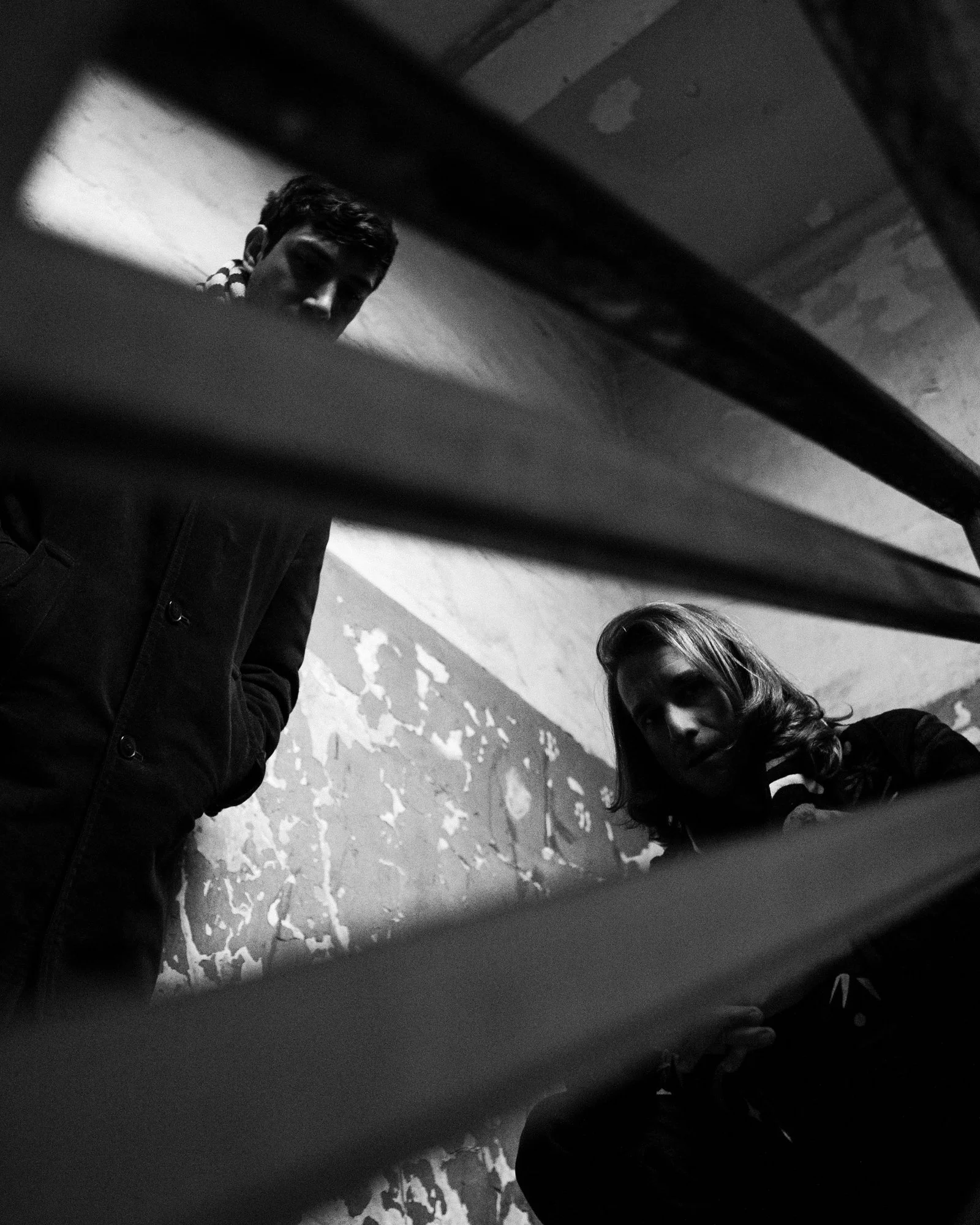 Black and white photo of two people standing and a third person’s head with long hair. The image is taken from a low angle, with a section of a surface visible in the foreground.