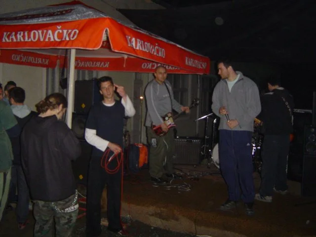 A group of men preparing a small music performance under an outdoor orange canopy.