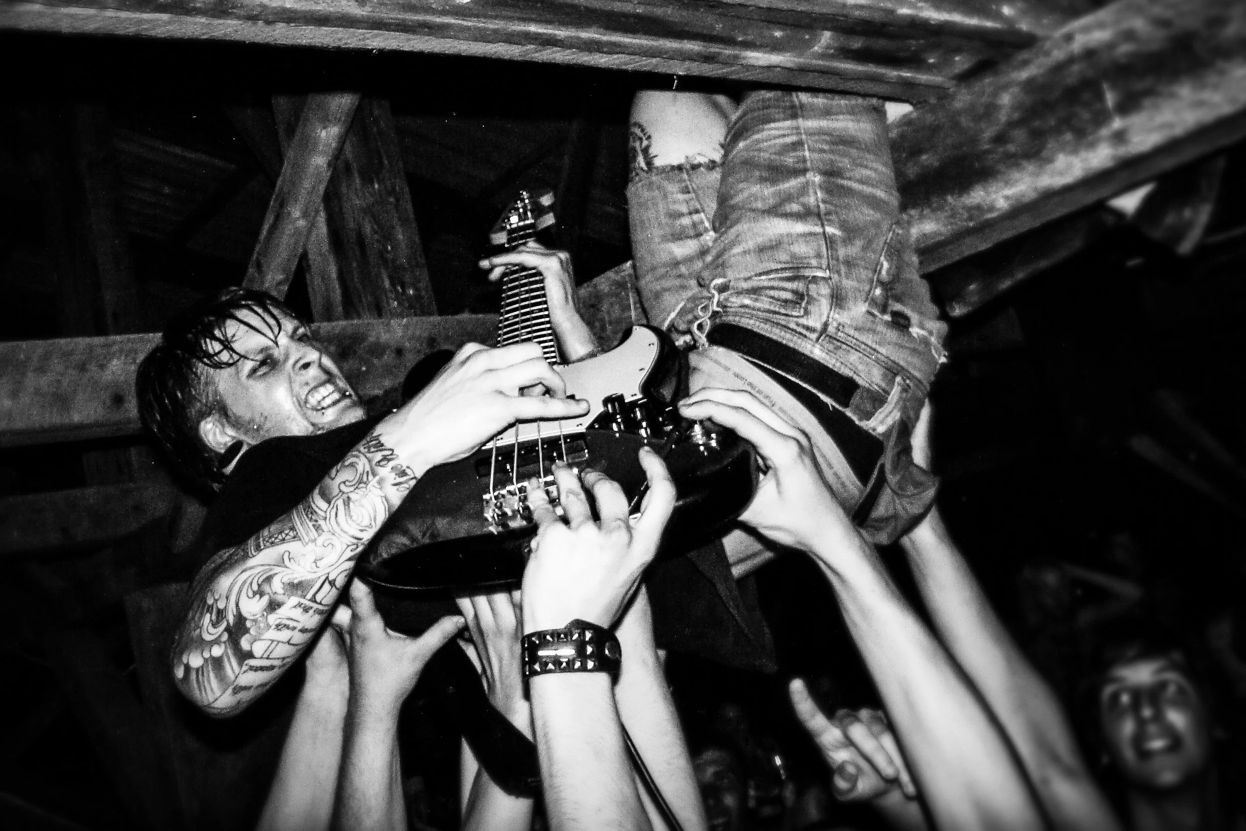 A person with tattoos on their arm playing an electric guitar while multiple hands reach up towards the instrument in a crowded, dark setting. Band name: Another Breath