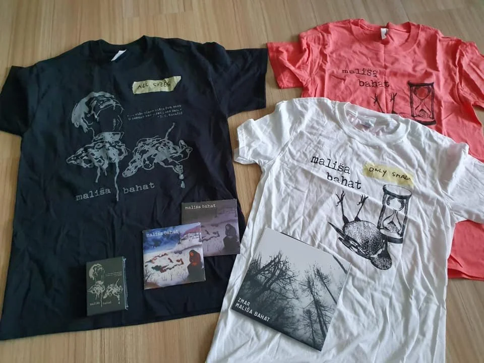 Three T-shirts in black, white, and pink, each with a design and the phrase 'malisa bahat.' The black T-shirt features a graphic of two mice and a cat. The pink T-shirt has a graphic of an hourglass, and the white T-shirt shows a stylized snail and a