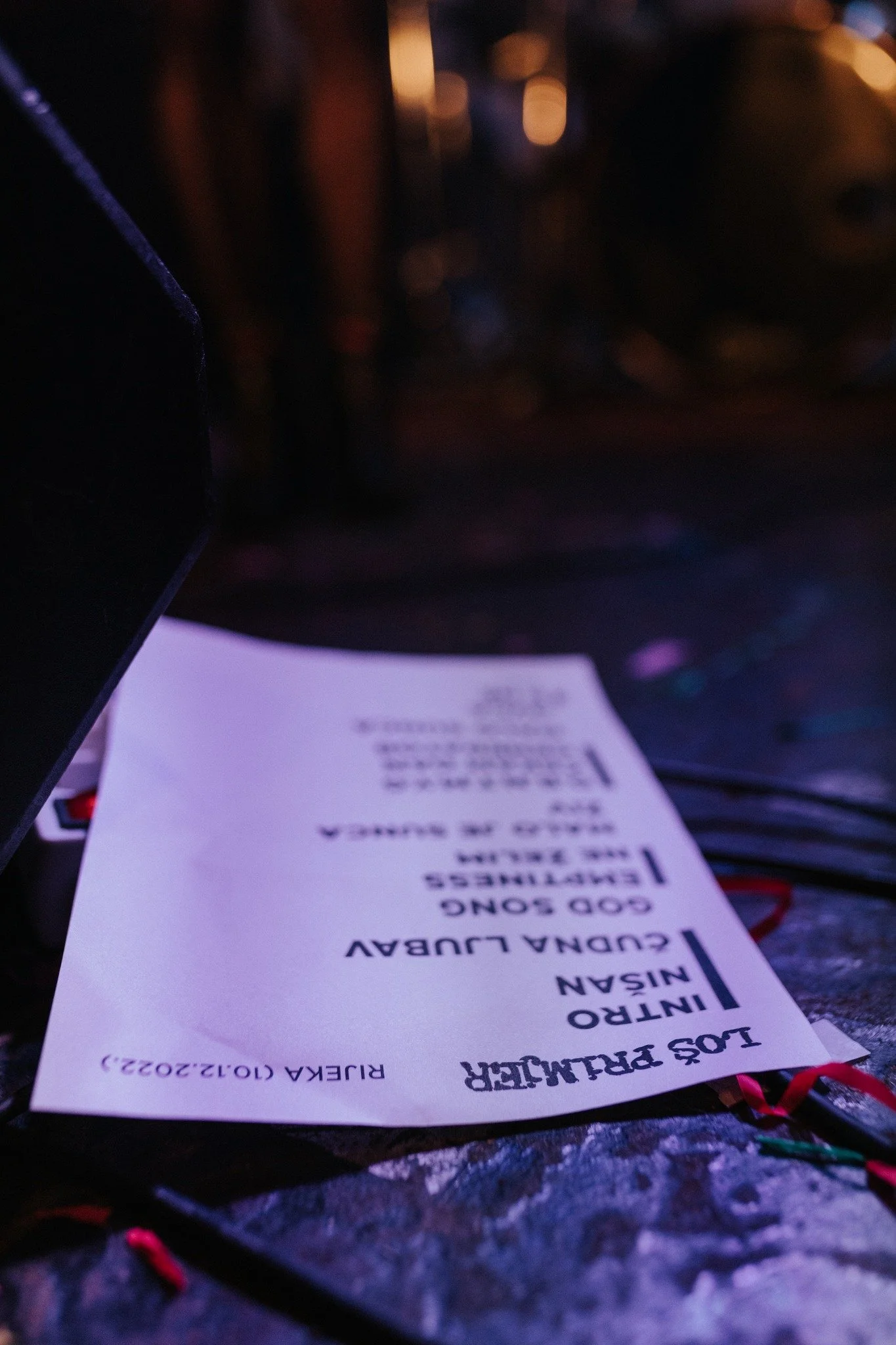 A paper receipt on a dark surface, with text in black ink, partially in focus, surrounded by colorful objects and a black electronic device.
