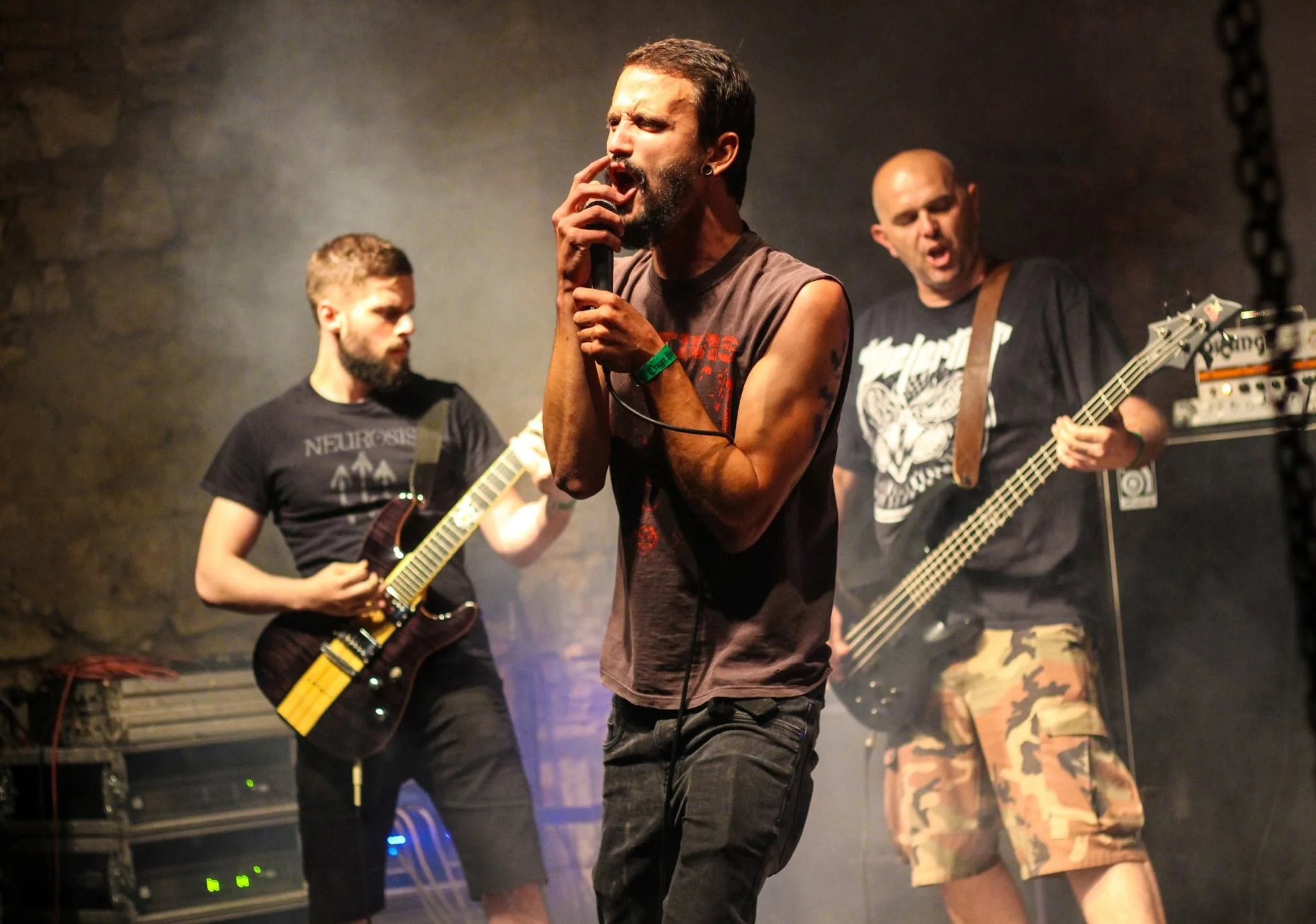 A band performing on stage with a vocalist holding a microphone, a guitarist, and a bassist.