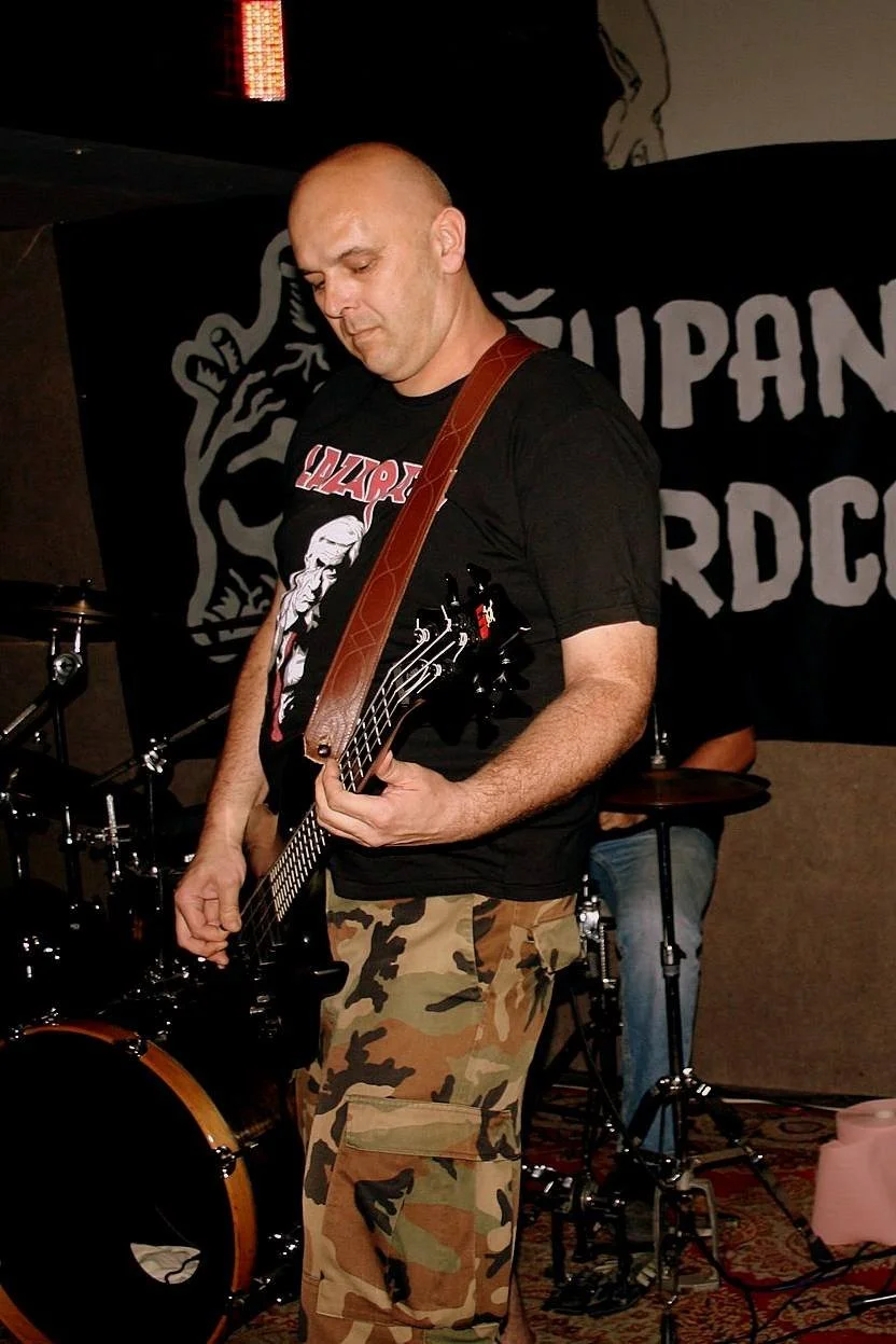 A man playing an electric guitar during a band performance, with a drum set in the background and a banner.