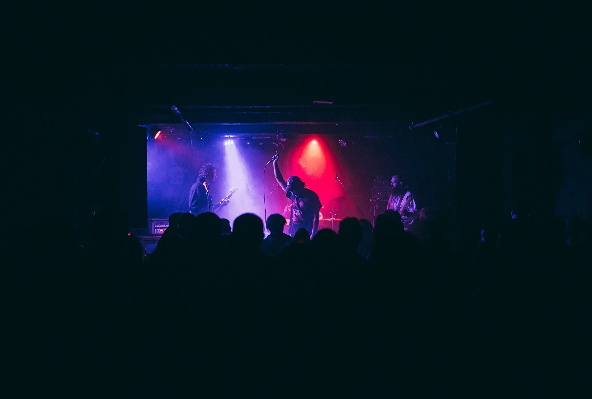 A band performing on stage under colorful lights with an audience watching in the dark.