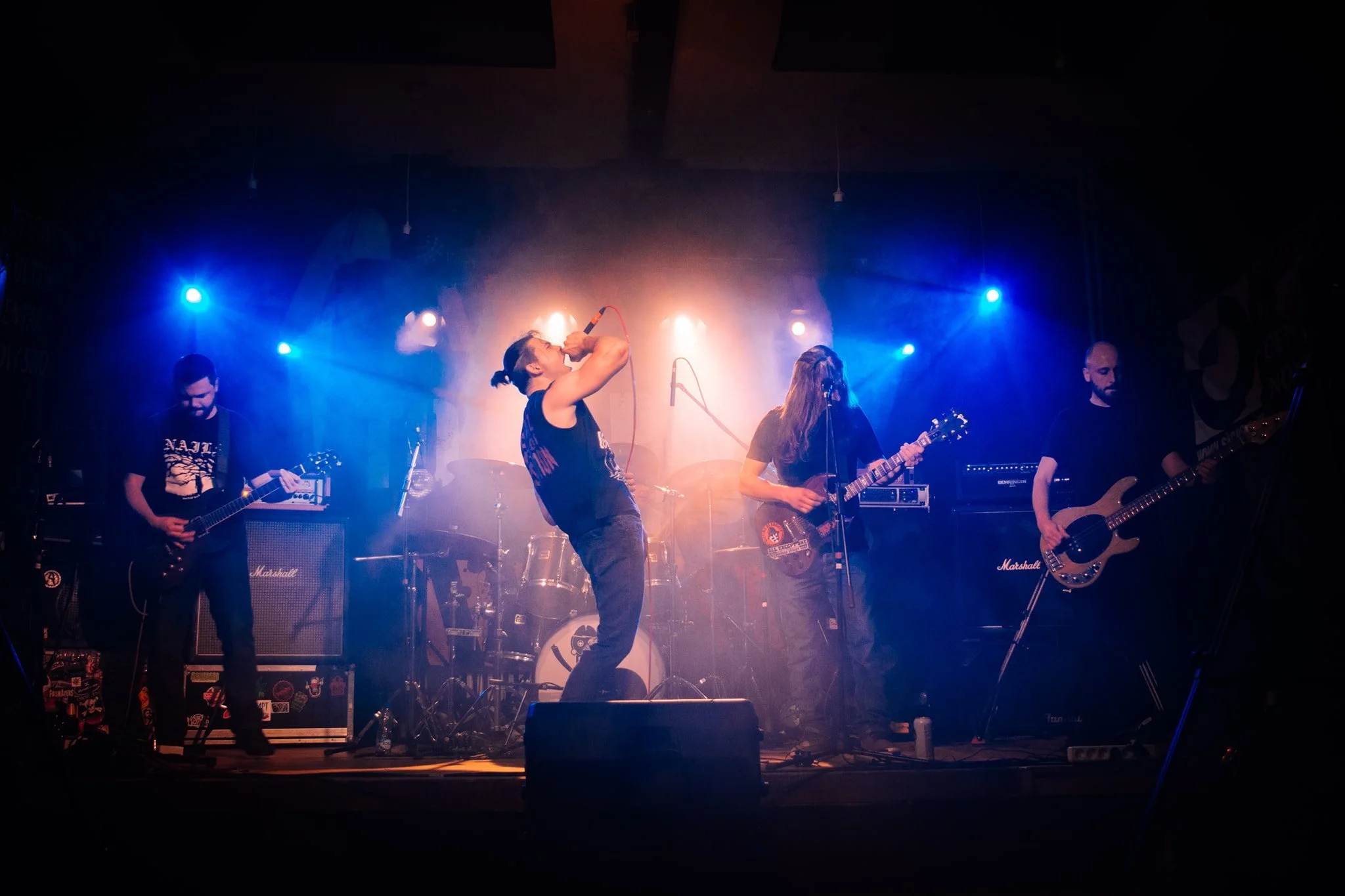 A band performing on stage with multiple musicians playing guitars and singing, illuminated by vibrant blue and warm stage lights.