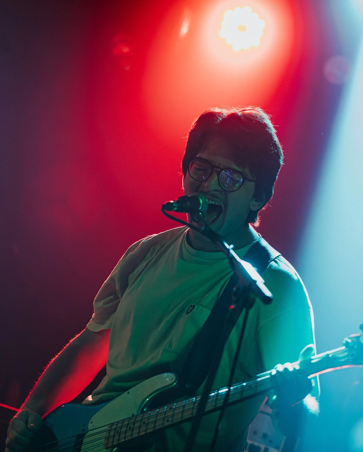 A person singing into a microphone while playing an electric guitar on stage with vibrant red, blue, and white lighting.