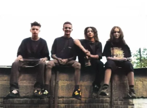 Four young people sitting on a brick ledge outdoors, looking at the camera.