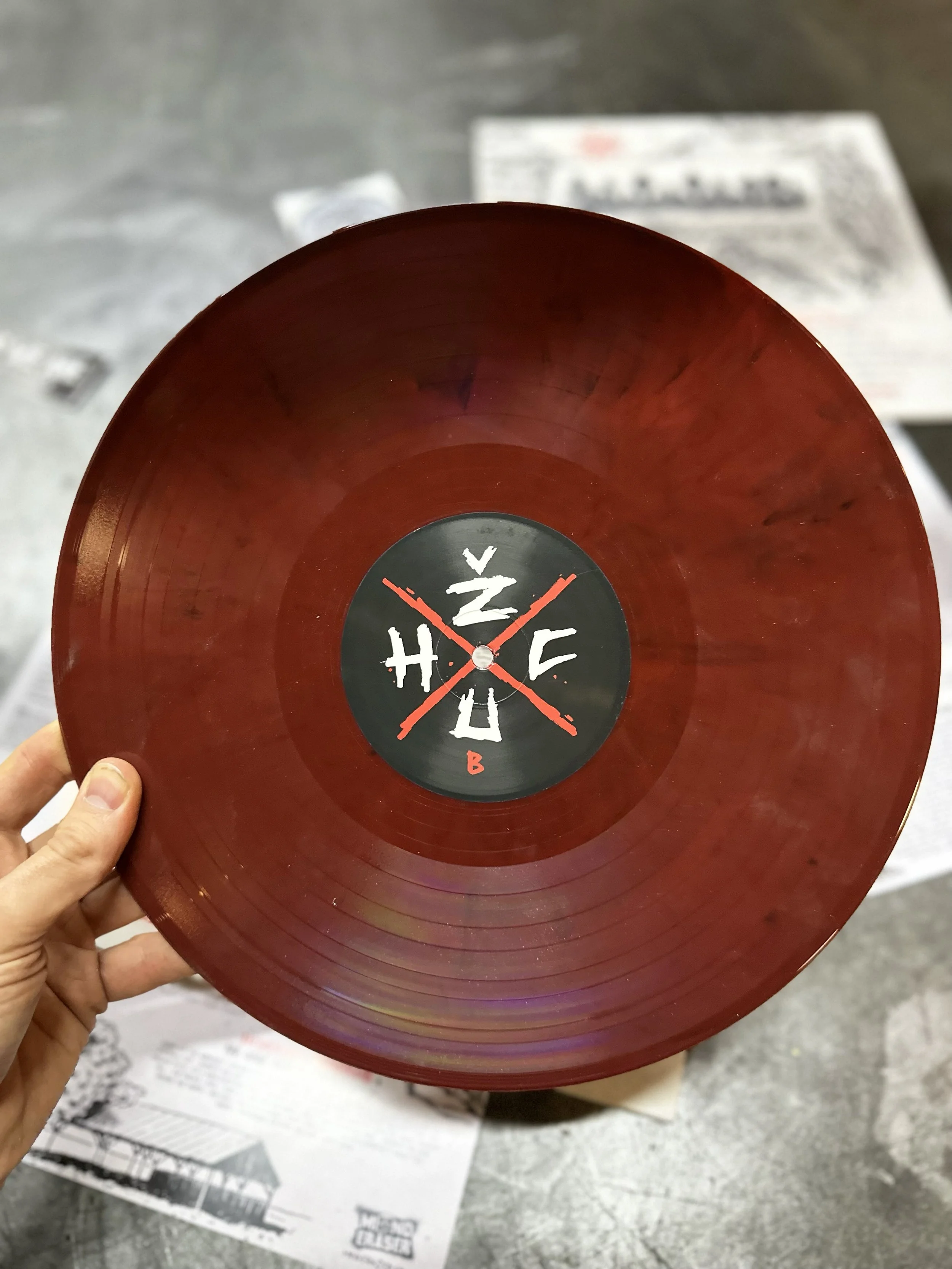 Red vinyl record with a black and white label featuring a design with crossed drumsticks.