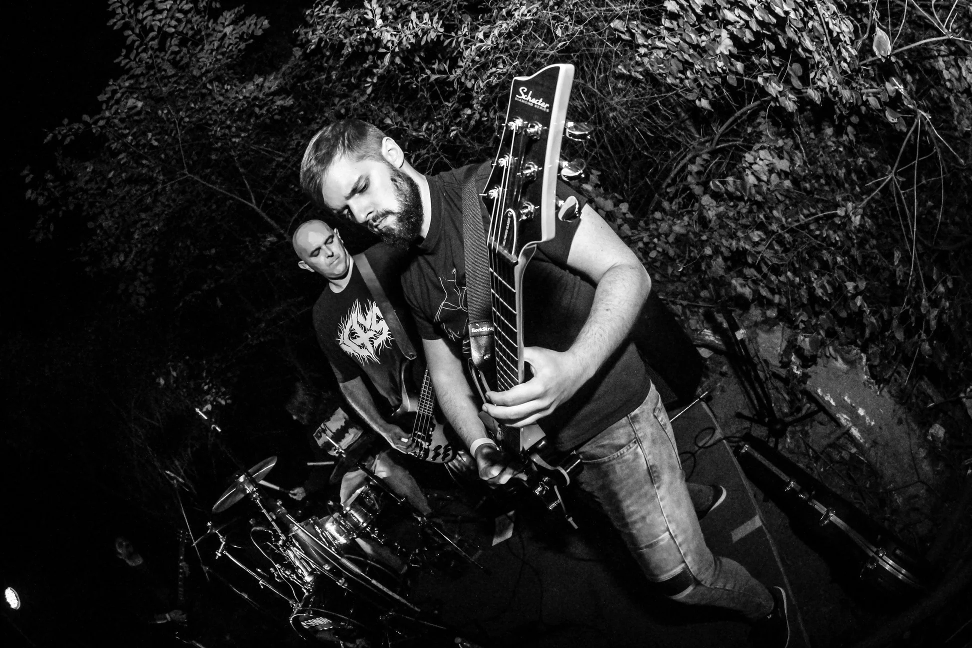Two men playing electric guitars during a performance at night, surrounded by trees and musical equipment.
