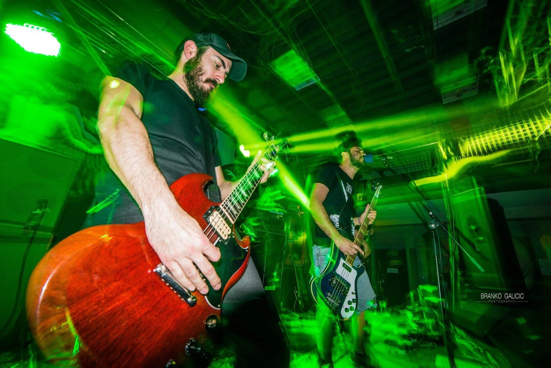 Two musicians playing electric guitars on stage with green laser lighting and fog effects. Band name: 1000mods
