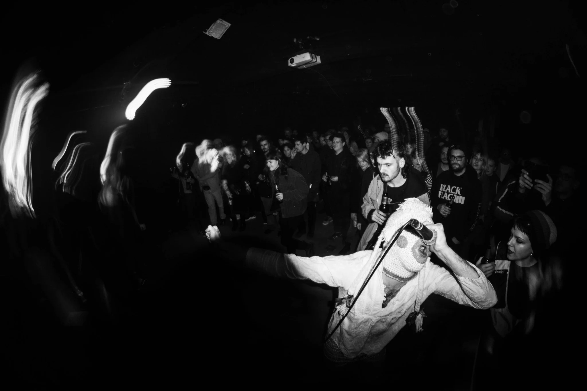 A crowd of people at a concert or event in a dark venue, with some holding drinks and engaging with the performance.