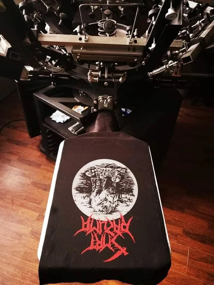 A tattoo machine complex with a cloth draped over the lower part, displaying an image of a wolf howling under a full moon and the words "Smrt Razuma" in red, stylized font.