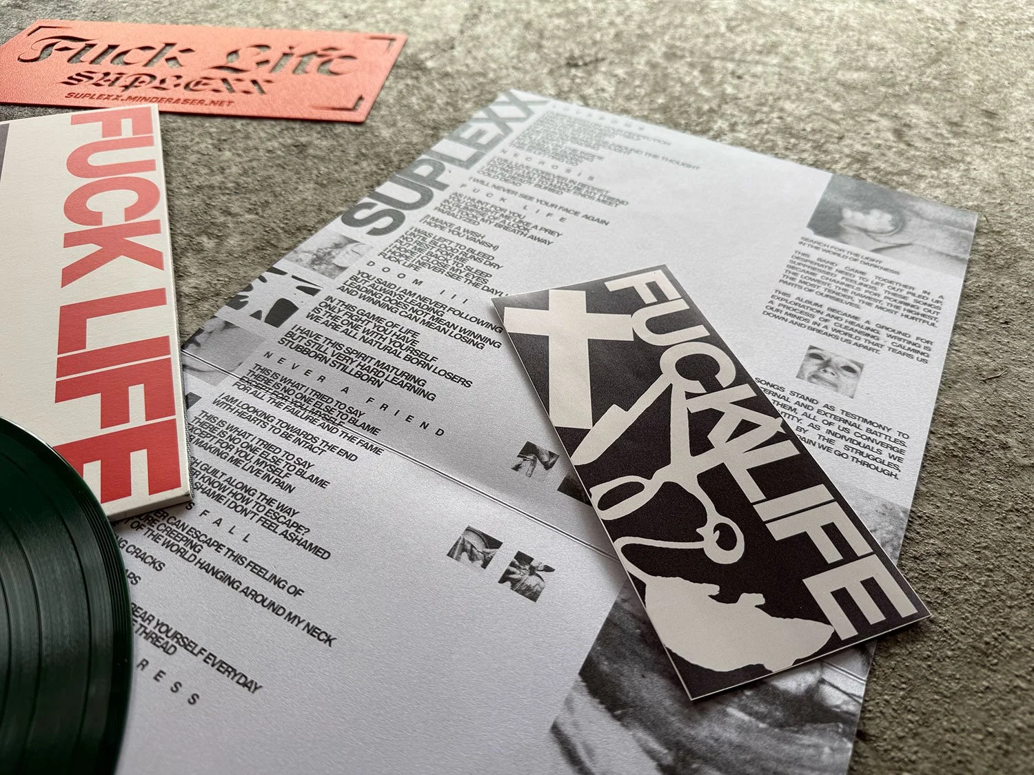 Music album, lyric sheets, sticker, and vinyl record on a concrete surface.