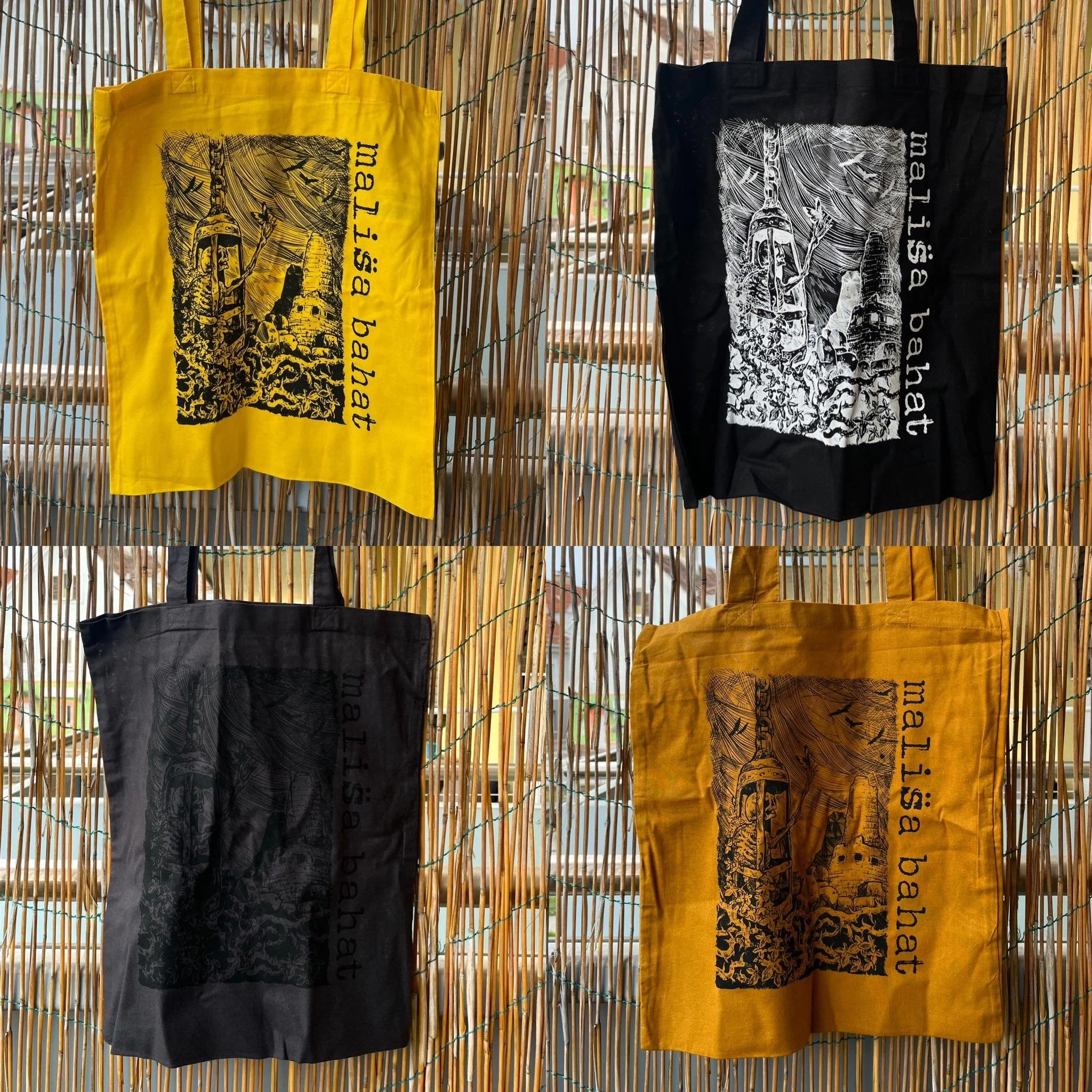 Two tote bags hanging on a bamboo fence; one yellow and one black, both featuring a graphic design of a tower or castle with surrounding foliage and the text 'Thailand'.