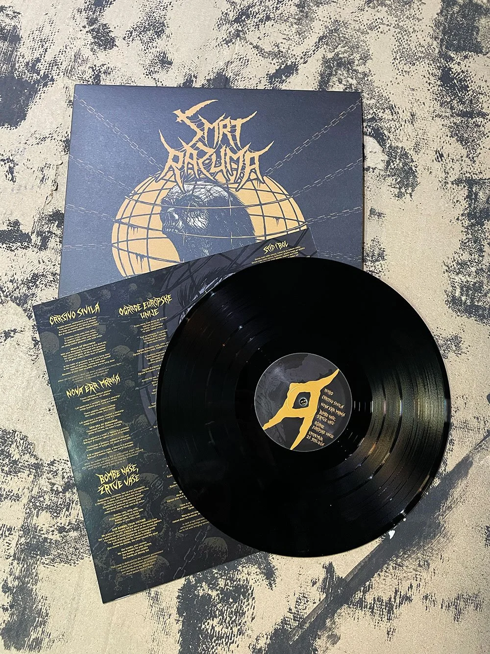 A black vinyl record partially on top of two album covers, one with a mythological creature and another with tracklist text, all on a textured surface.