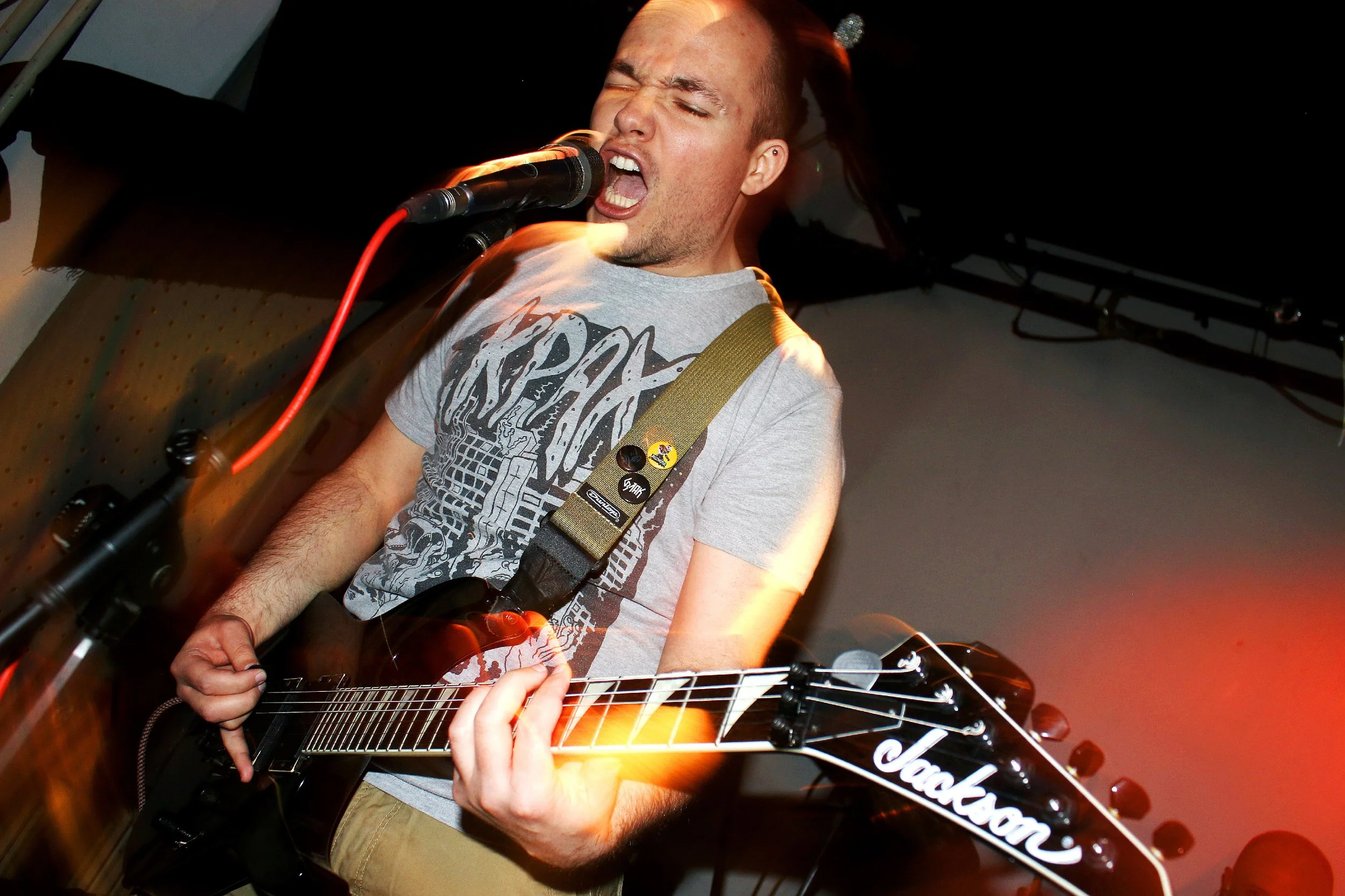 Person performing with a guitar on stage, singing passionately into a microphone.