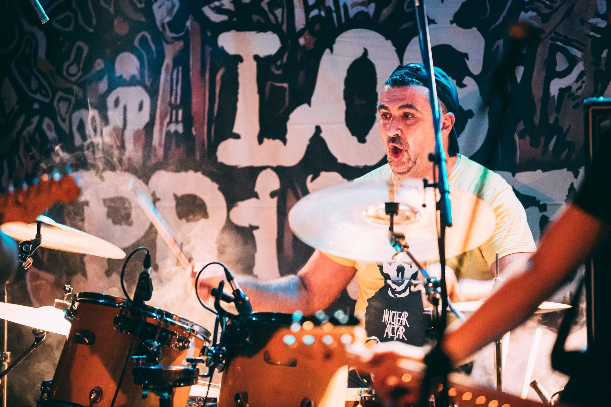 A man playing drums, with a passionate expression, in a room with graffiti-style wall art.