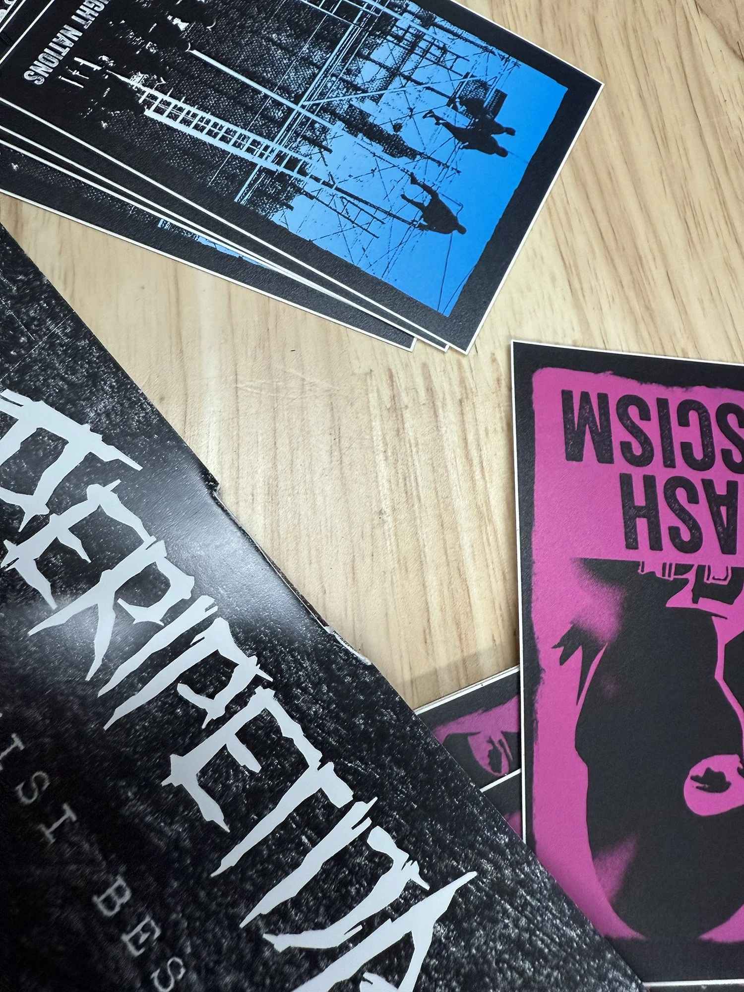 Stack of printed flyers or posters on a wooden surface, featuring various graphic designs and text, including images of people on swings and bold text in different colors.