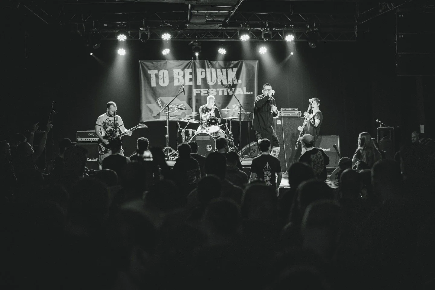 Black and white photo of a band performing on stage at a punk festival, with the crowd in the foreground