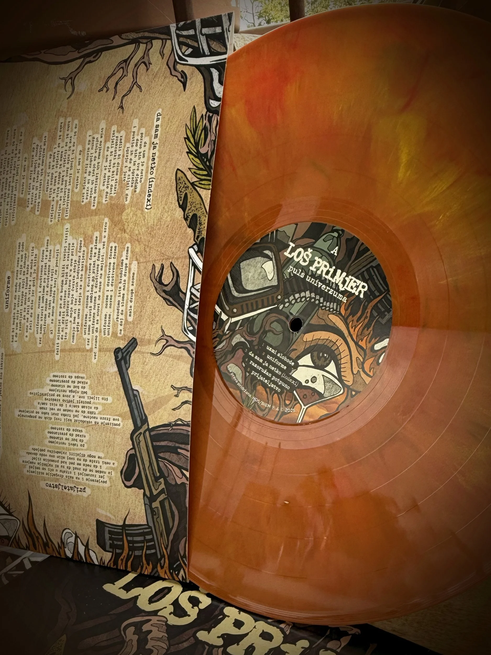 Close-up of a stylized illustration featuring a tree, a gun, and a cassette tape. The image appears to be part of a display or poster. There is a partially visible text that reads 'PULS UNIVERZUMA'.
