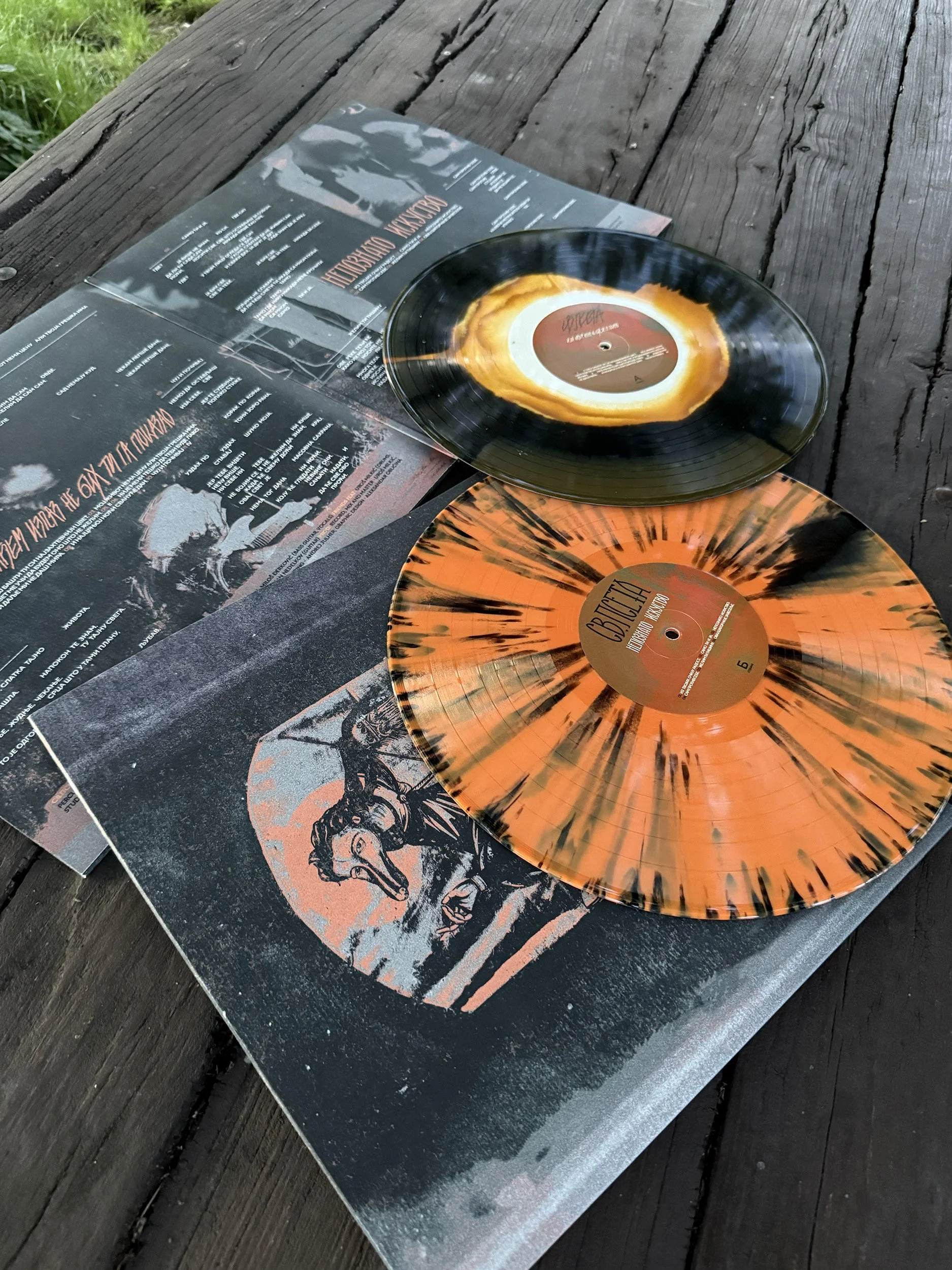 Black vinyl records with colorful splatter patterns, placed on a weathered wooden surface.