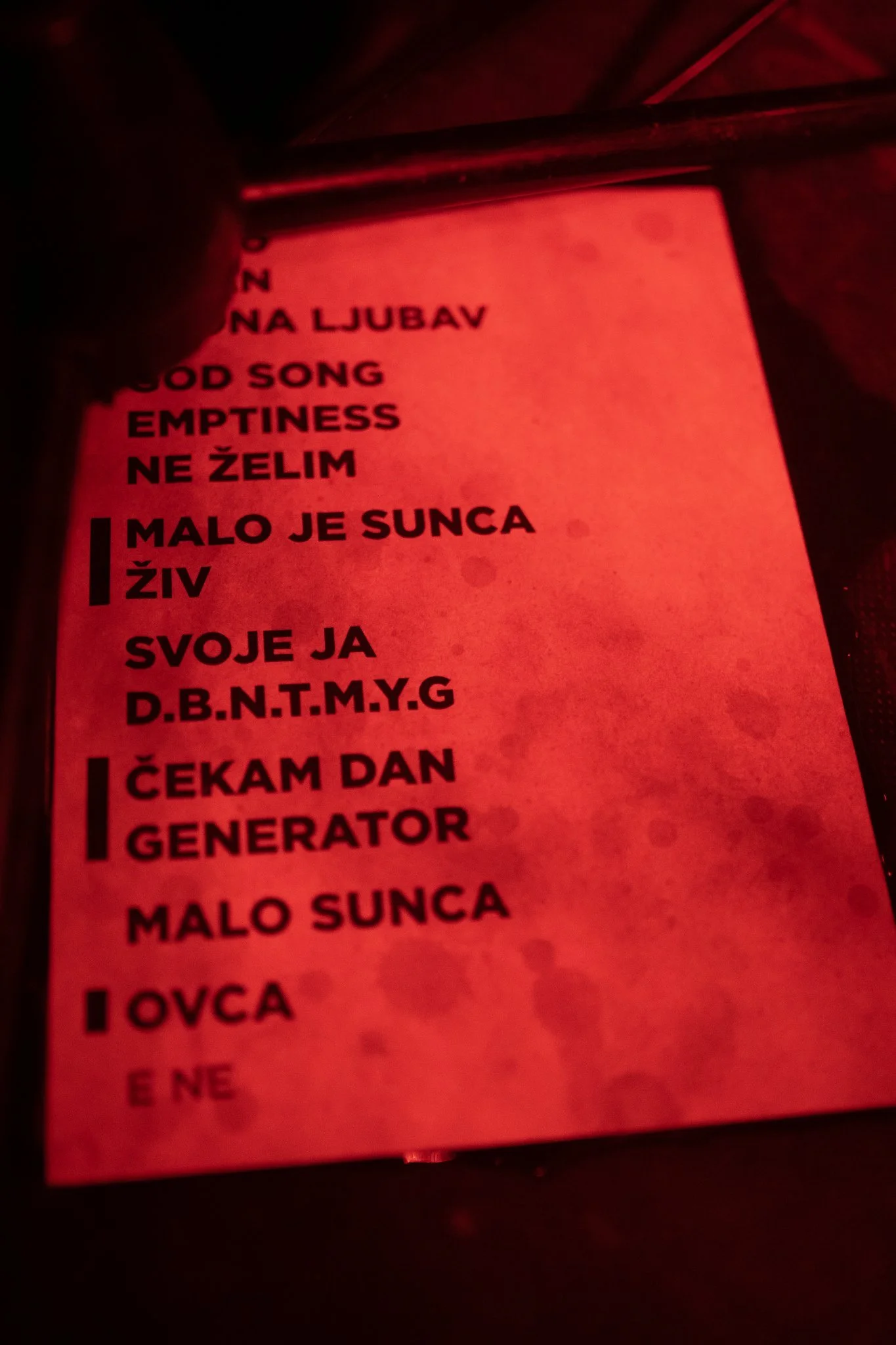 Close-up of a red-lit screen displaying a list of words in Serbian or Croatian, with some words in English such as 'GOD SONG' and 'EMPTINESS'.