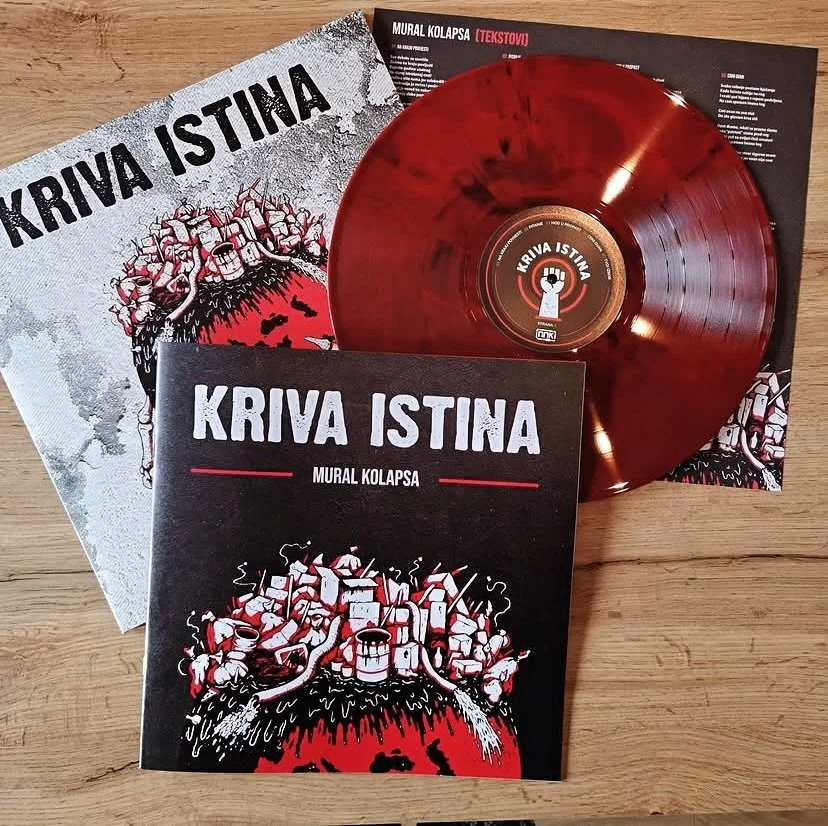 A red vinyl record, a booklet, and a music album cover titled 'Kriva Istina' by Mural Kolapsa, all placed on a wooden surface.