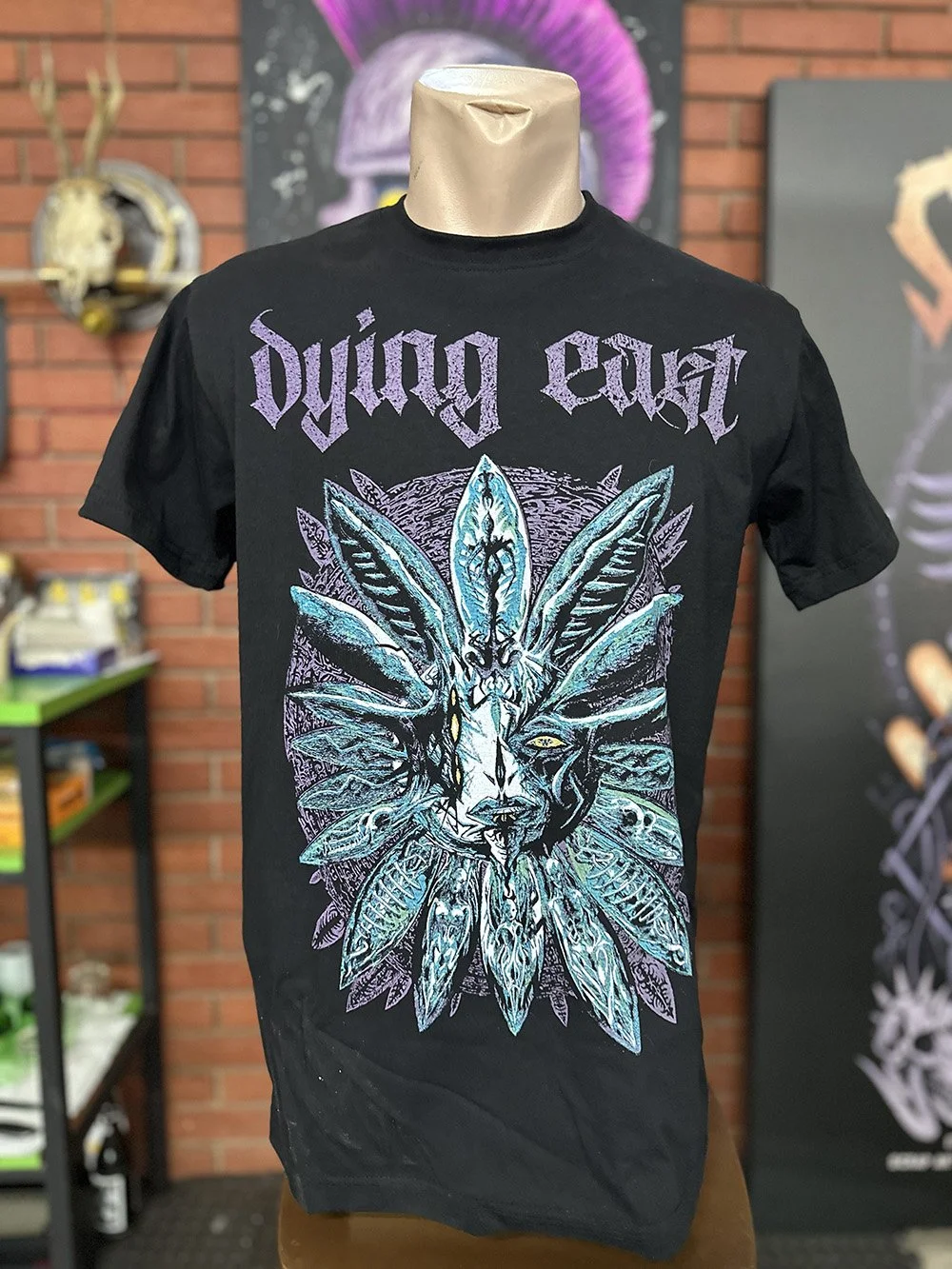 Black T-shirt with the words 'dying east' in purple at the top and a large colorful graphic of a fox with feathers on its face and head, surrounded by feathers.