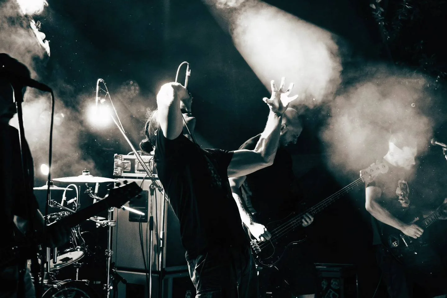 Band performing on stage with guitarist, bassist, and singer, with stage lights and smoke effects, in black and white.