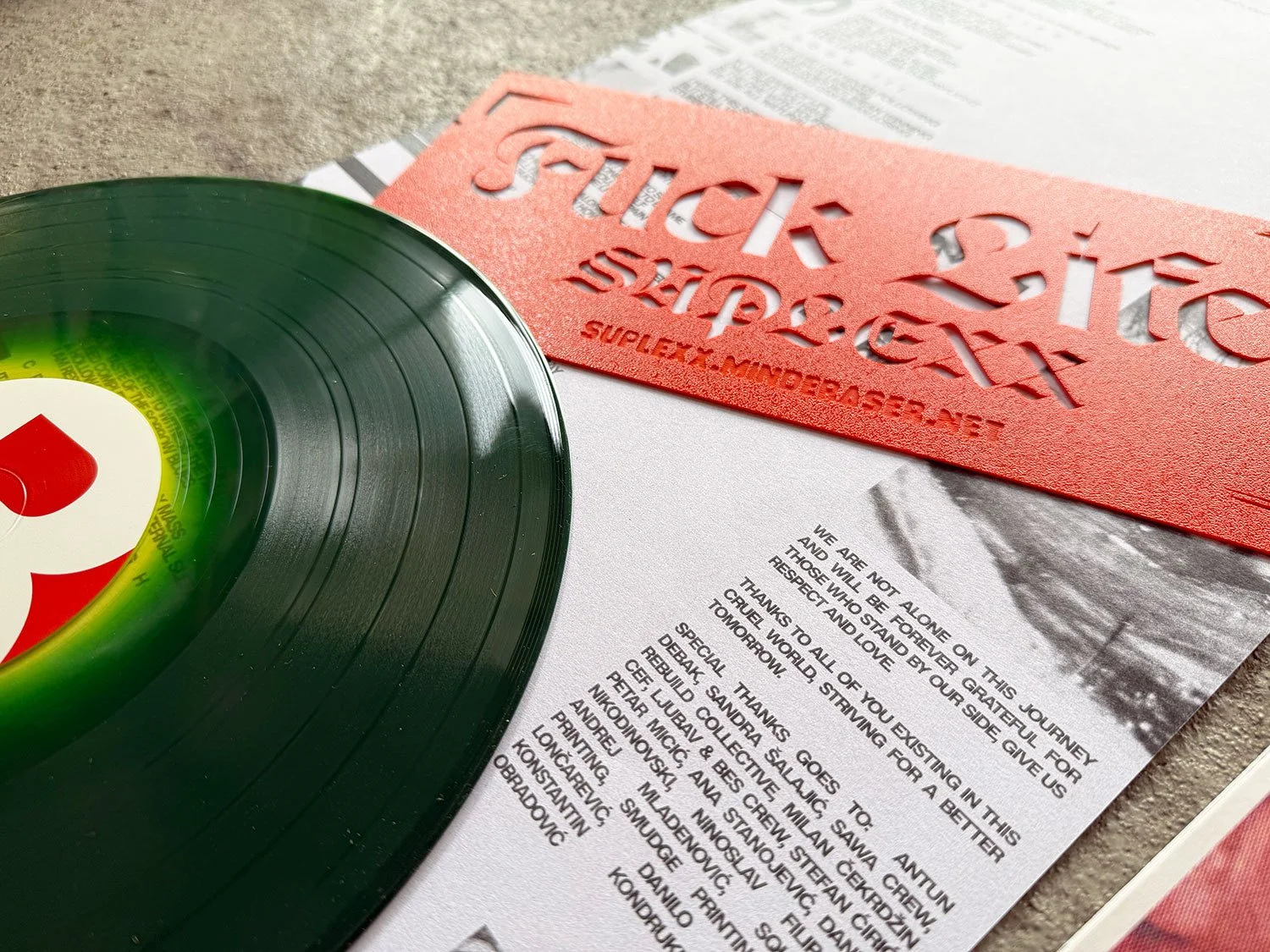 A black vinyl record, a red stencil, and a printed document on a textured surface.