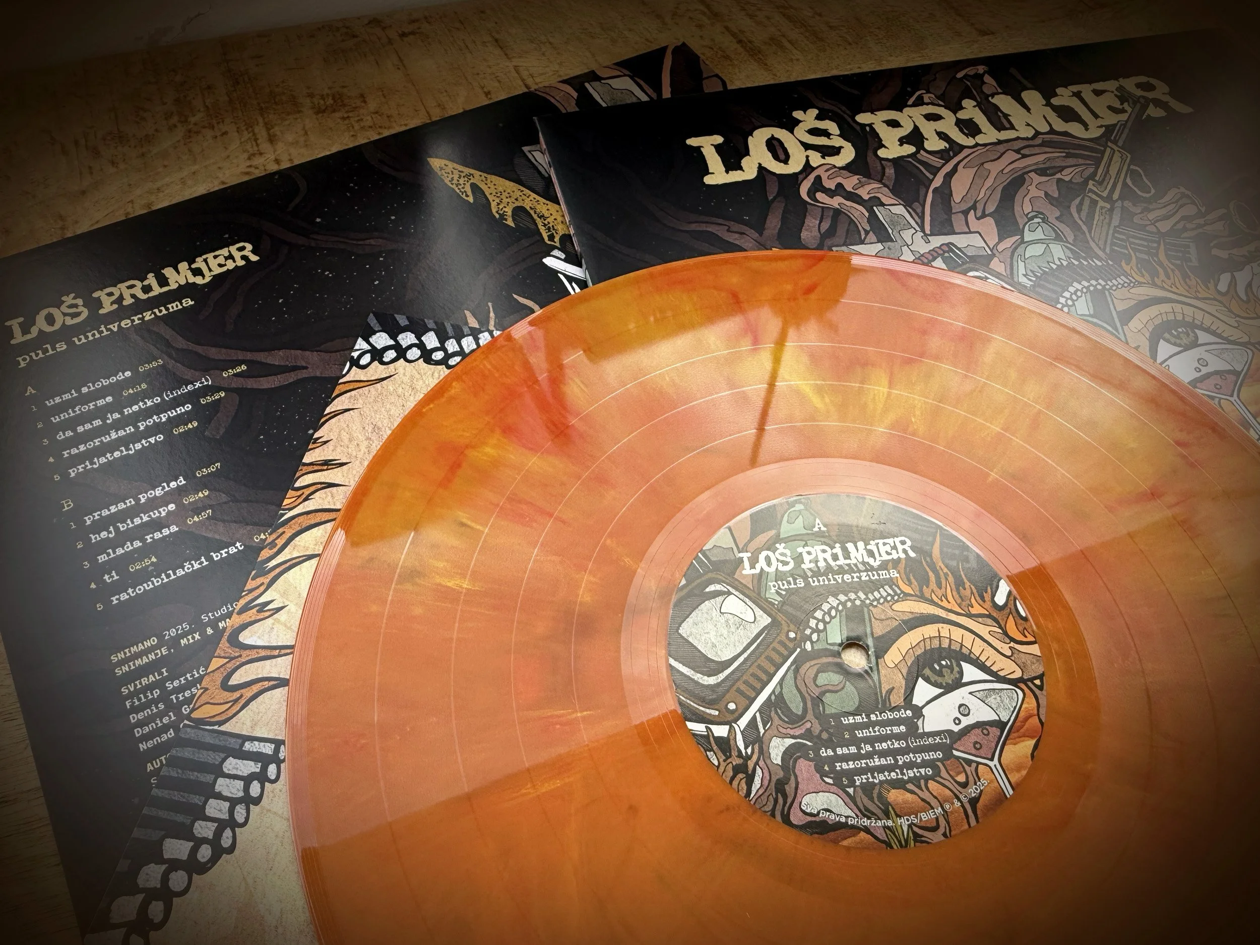 Part of a vinyl record and album cover for Los Prijamer's album titled 'Puls Univerzuma,' with colorful, detailed artwork and a tracklist in a different language.